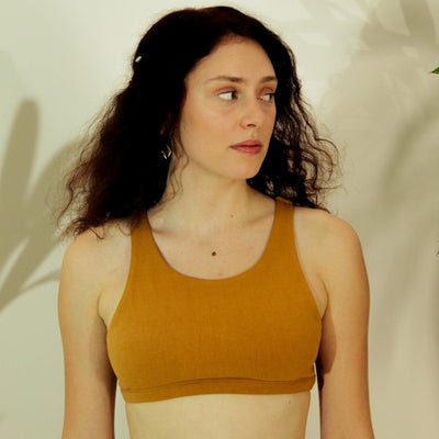 Woman wearing a mustard yellow tank top against a neutral background