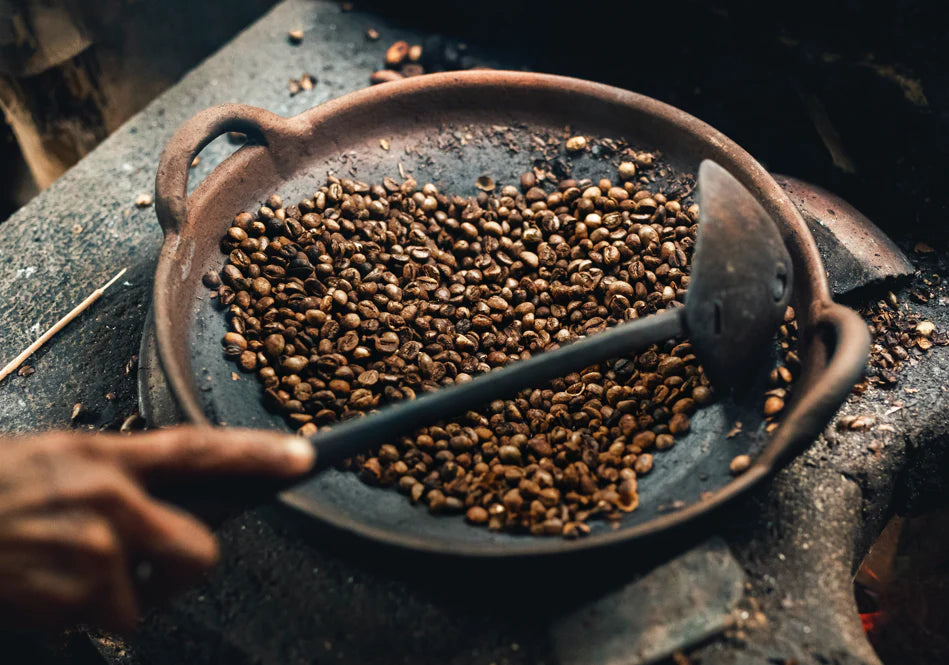 Hand holding a spoon over a pan of roasted coffee beans