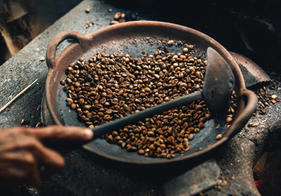 Hand holding a spoon over a pan of roasted coffee beans