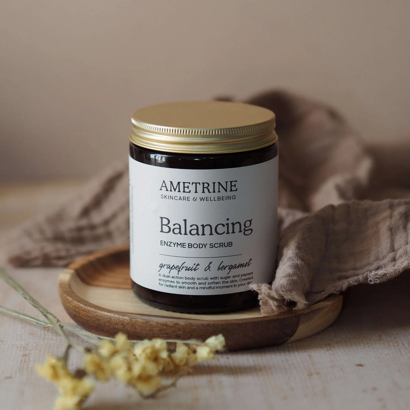 Ametrine Balancing Enzyme Body Scrub jar on a wooden tray with a neutral background