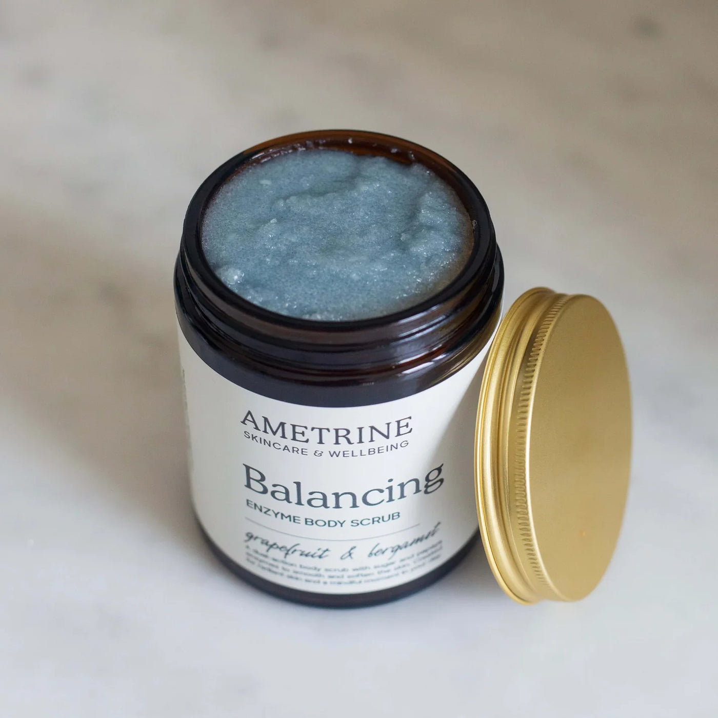 Ametrine Balancing Enzyme Body Scrub jar with gold lid on a light background