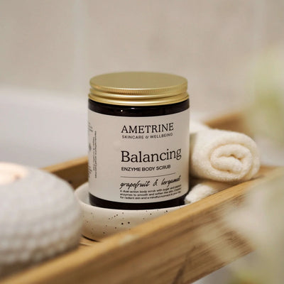 Ametrine Balancing Enzyme Body Scrub on a wooden shelf with towels.