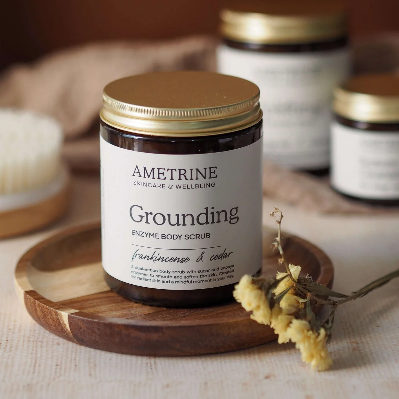 Ametrine Grounding Enzyme Body Scrub jar on a wooden tray with dried flowers.