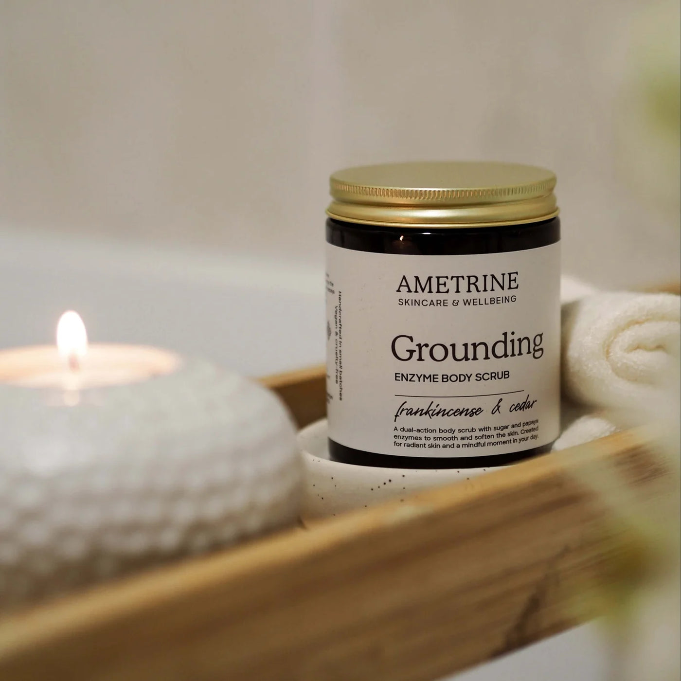 Ametrine Grounding Enzyme Body Scrub with a candle and towel in the background