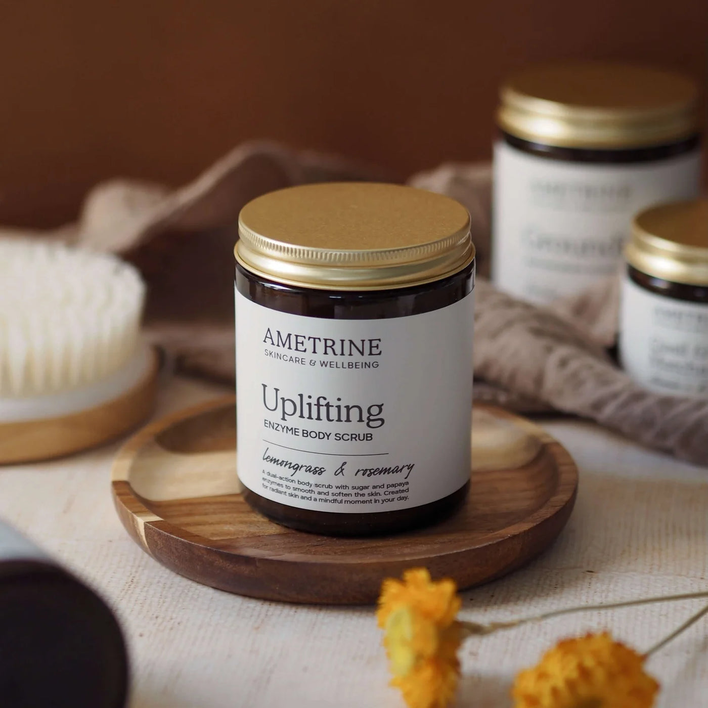 Ametrine uplifting body scrub jar on a wooden tray with a blurred background