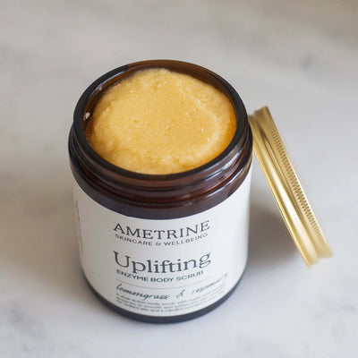 Ametrine Skincare & Wellbeing Uplifting Enzyme Body Scrub with a gold comb on a light background