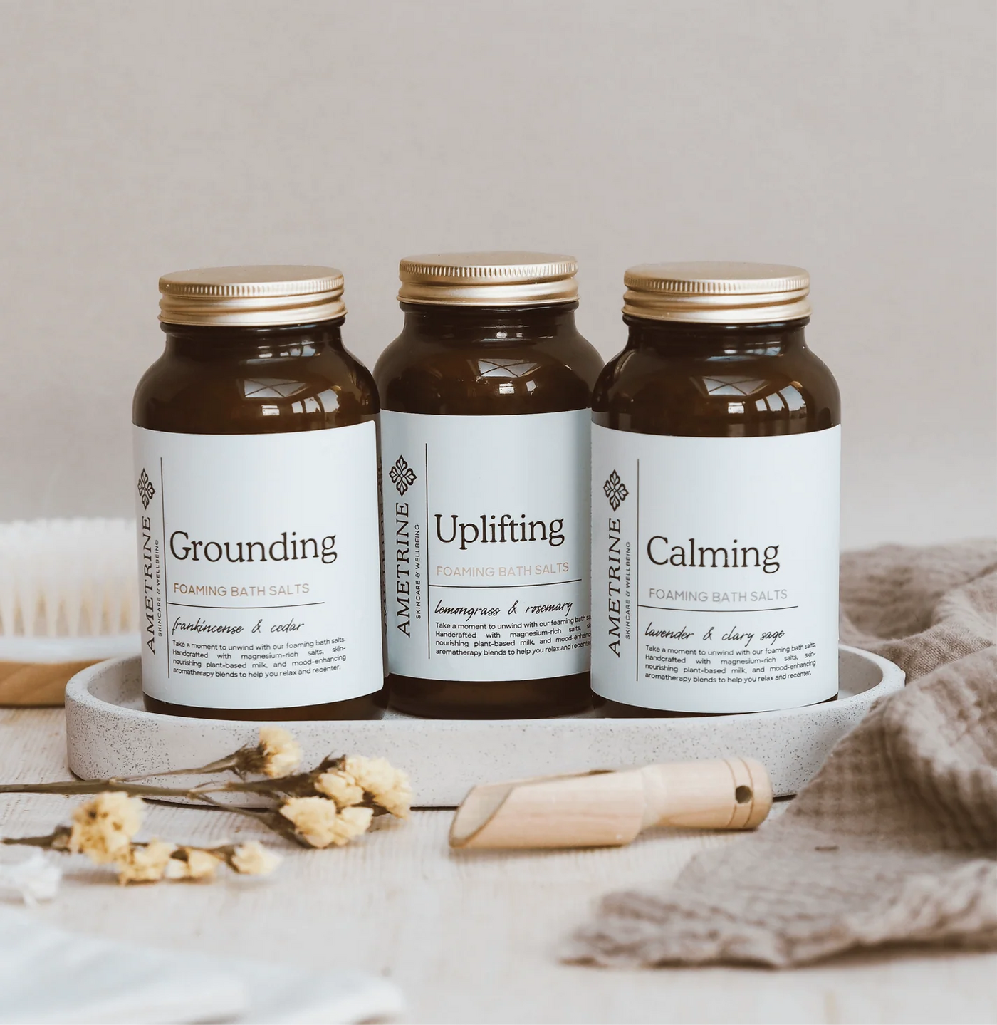 Three jars of Aromatherapy Associates bath salts labeled 'Grounding', 'Uplifting', and 'Calming' on a neutral background.