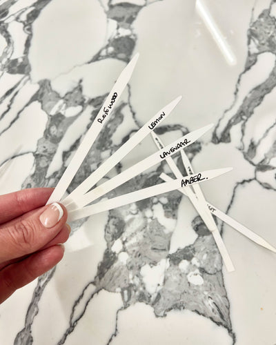 Hand holding white sticks with names written on them against a marble background
