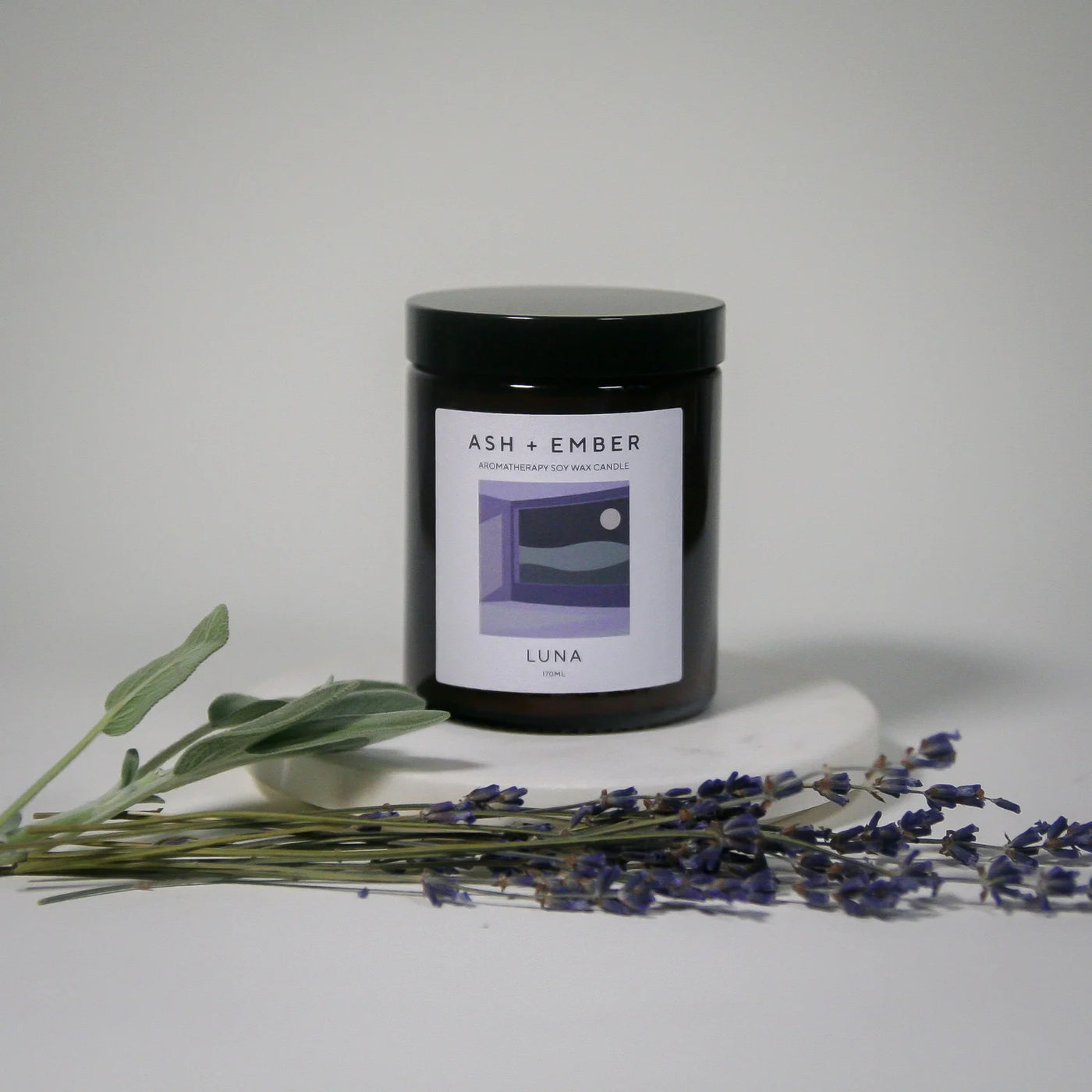 Candle labeled 'ASH + Ember Luna' with lavender and eucalyptus on a light background