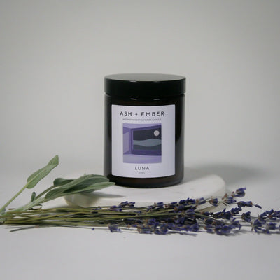 Candle labeled 'ASH + Ember Luna' with lavender and eucalyptus on a light background
