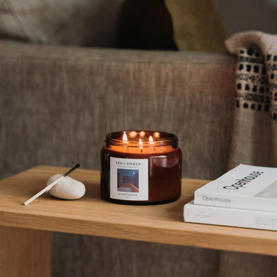 Candle on a wooden table with books and a remote control, blurred sofa in the background
