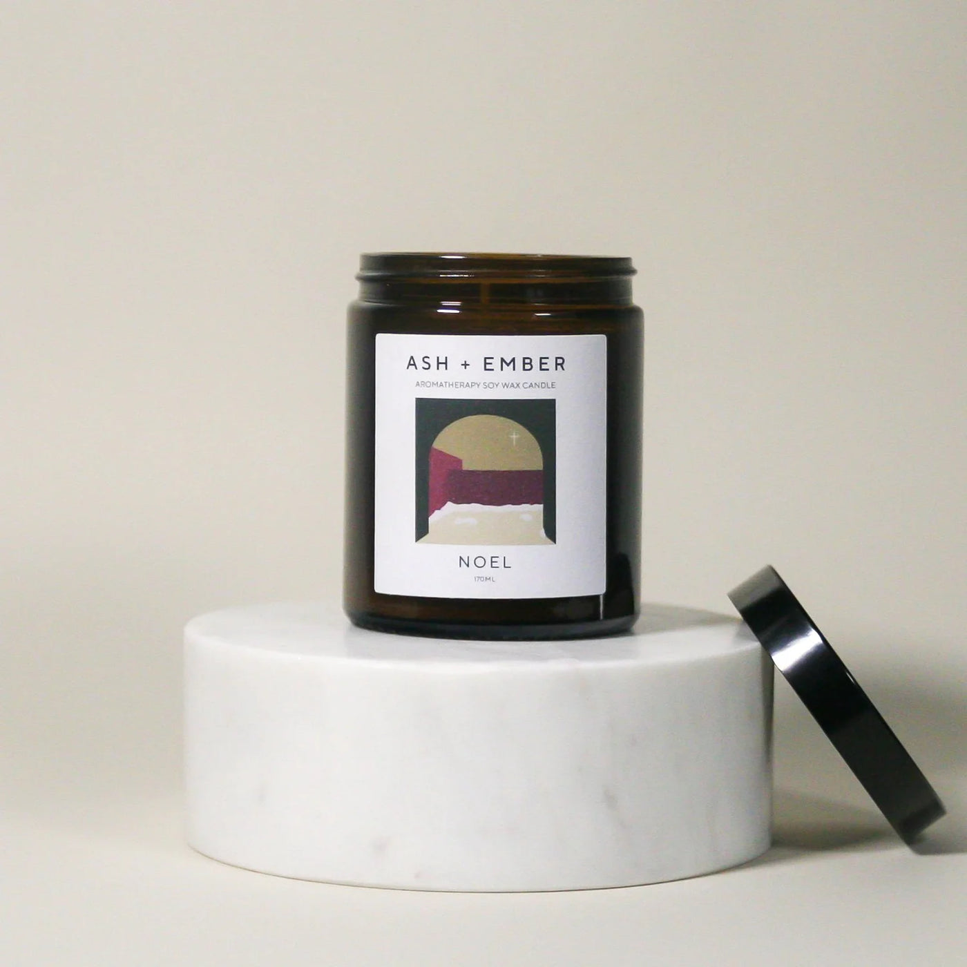 Candle jar labeled 'ASH + Ember' on a white surface with a neutral background
