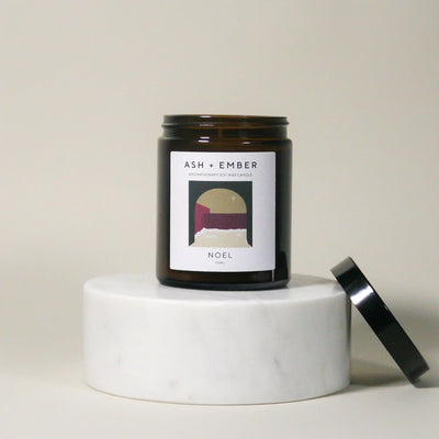Candle jar labeled 'ASH + Ember' on a white surface with a neutral background