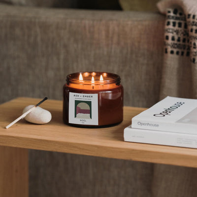 Candle with a label on a wooden table next to a book, with a blurred background