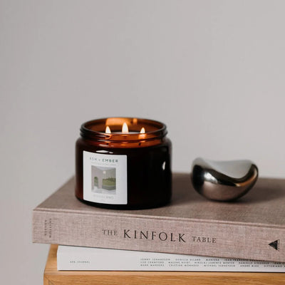 Candle in a black jar with an amber lid on top of a book titled 'The Kinfolk Table'.