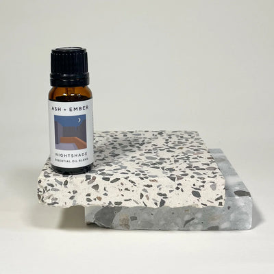 Essential oil bottle labeled 'Ash + Ember' on a terrazzo coaster with a white background