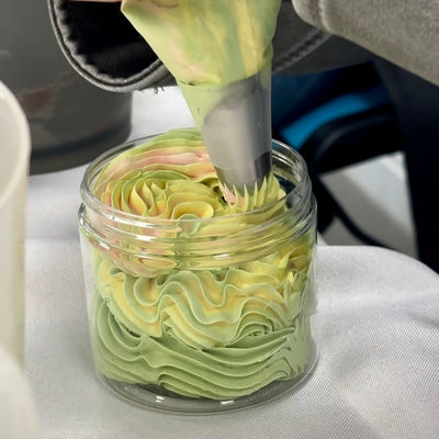 Person piping green frosting into a glass jar on a white surface