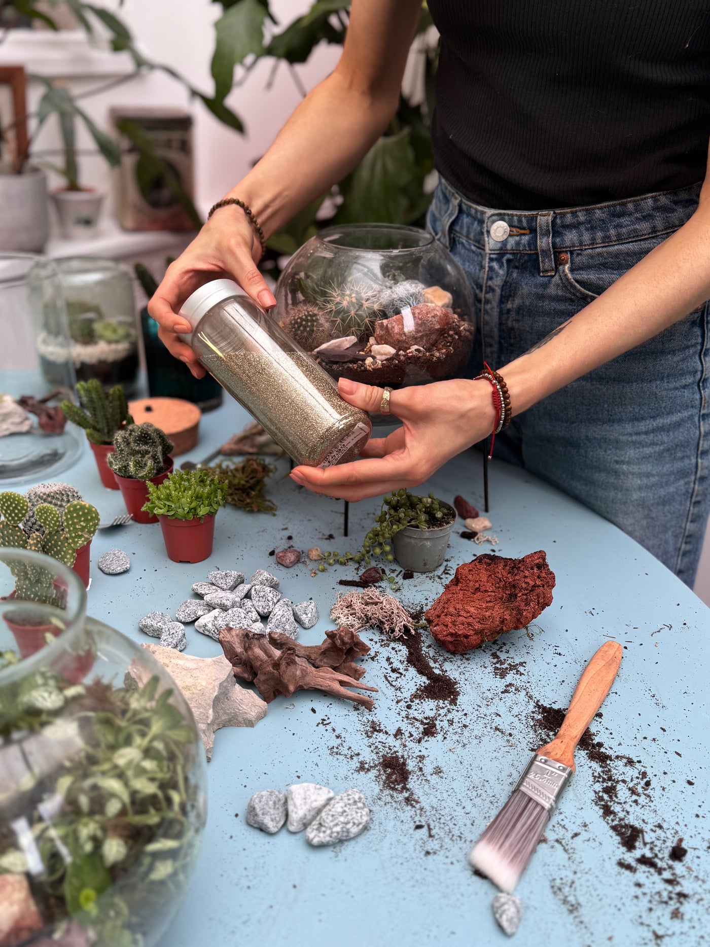 Person assembling a terrarium with various materials on a table