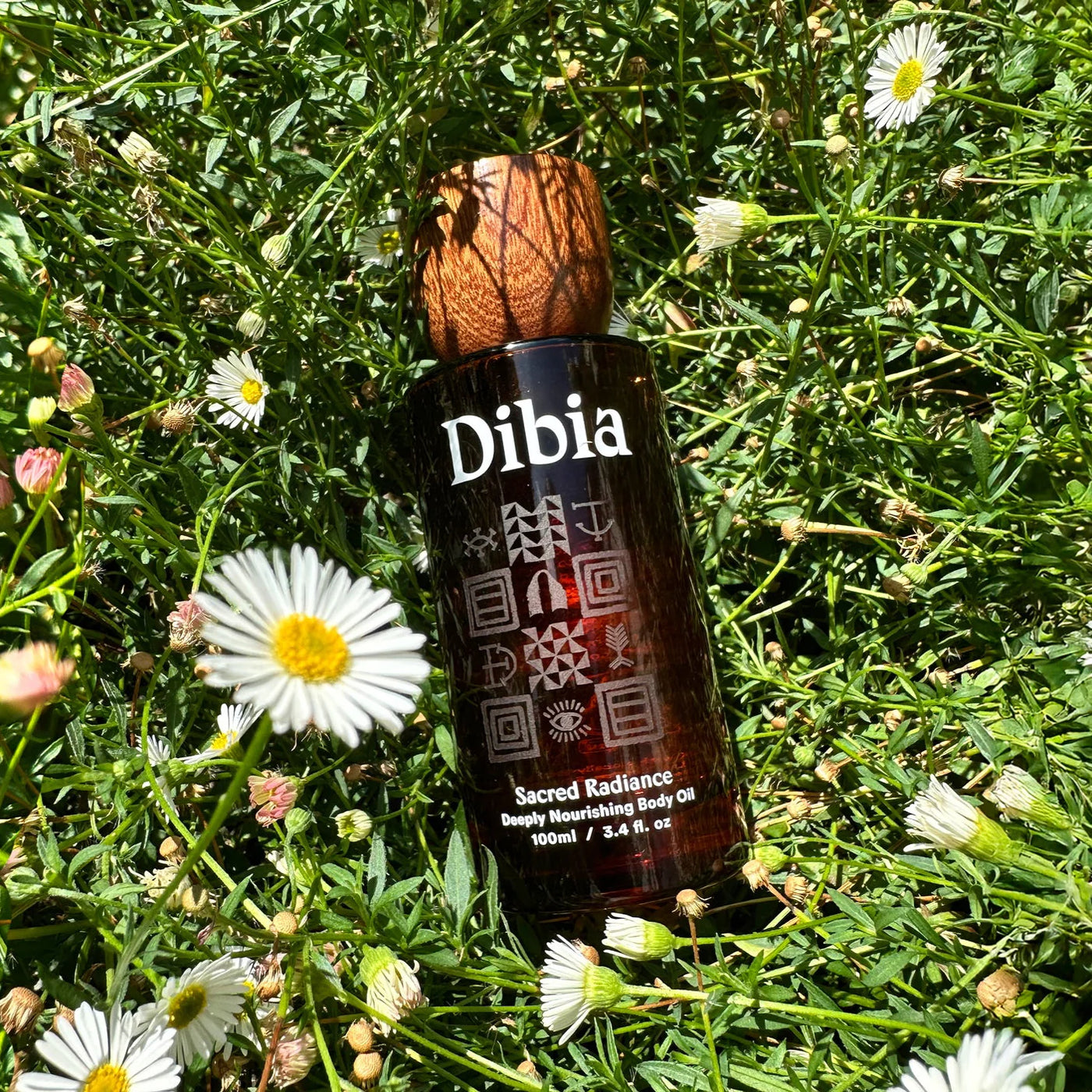 Dibia body oil bottle on grass with daisies