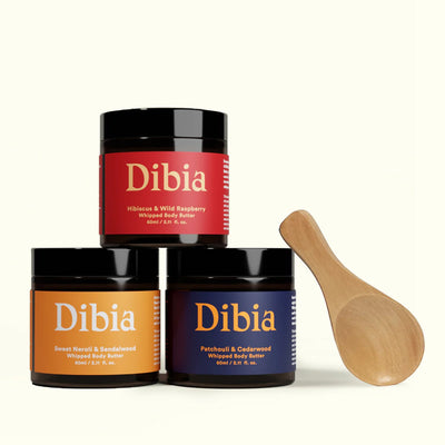 Three jars of Dibia whipped body butter with a wooden spoon on a white background
