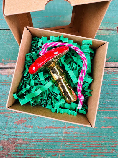 Decorative item with green ribbons and a gold and red object in a cardboard box on a teal wooden surface.