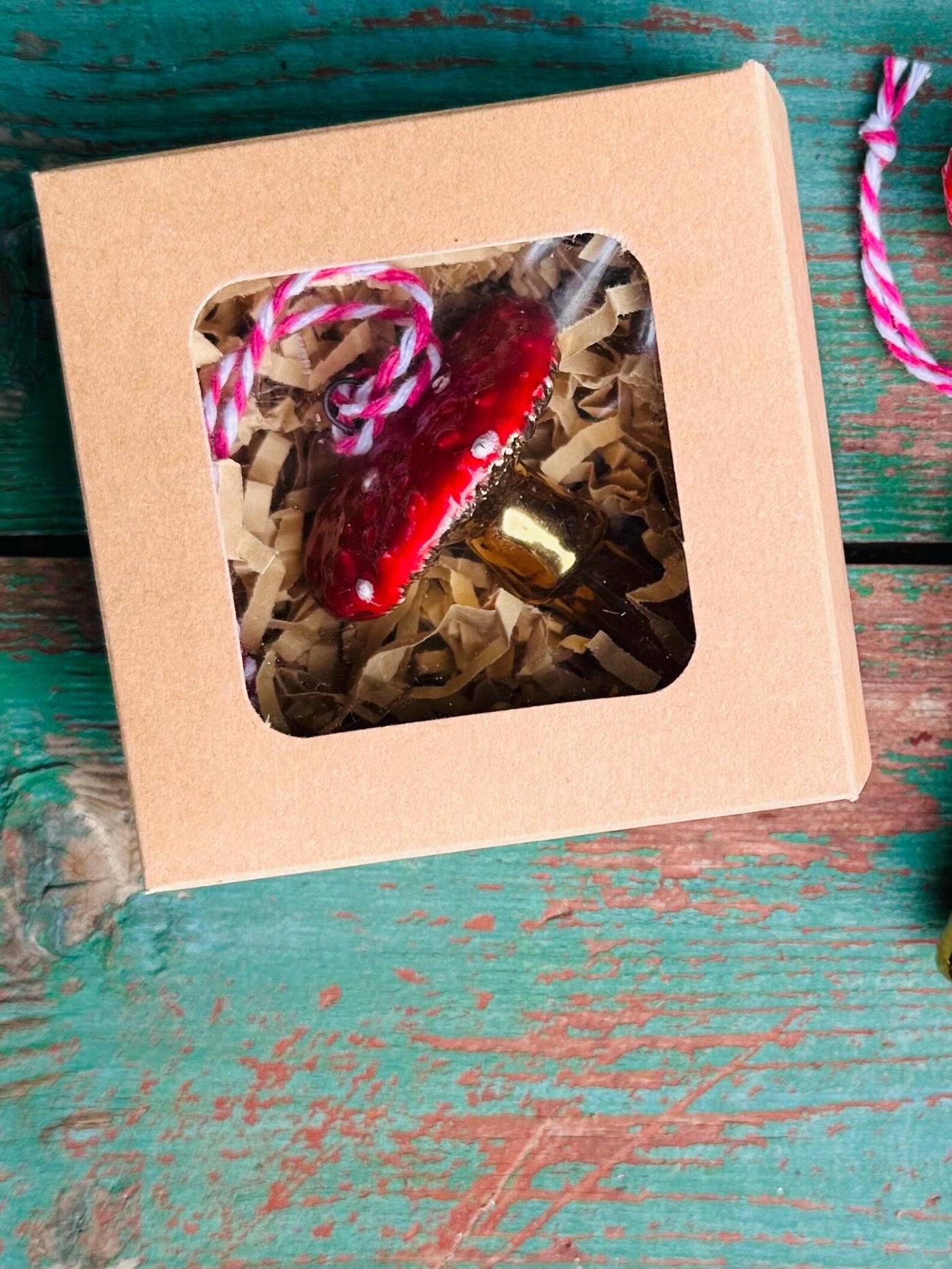 Red heart-shaped object with gold accents in a cardboard box on a rustic wooden surface