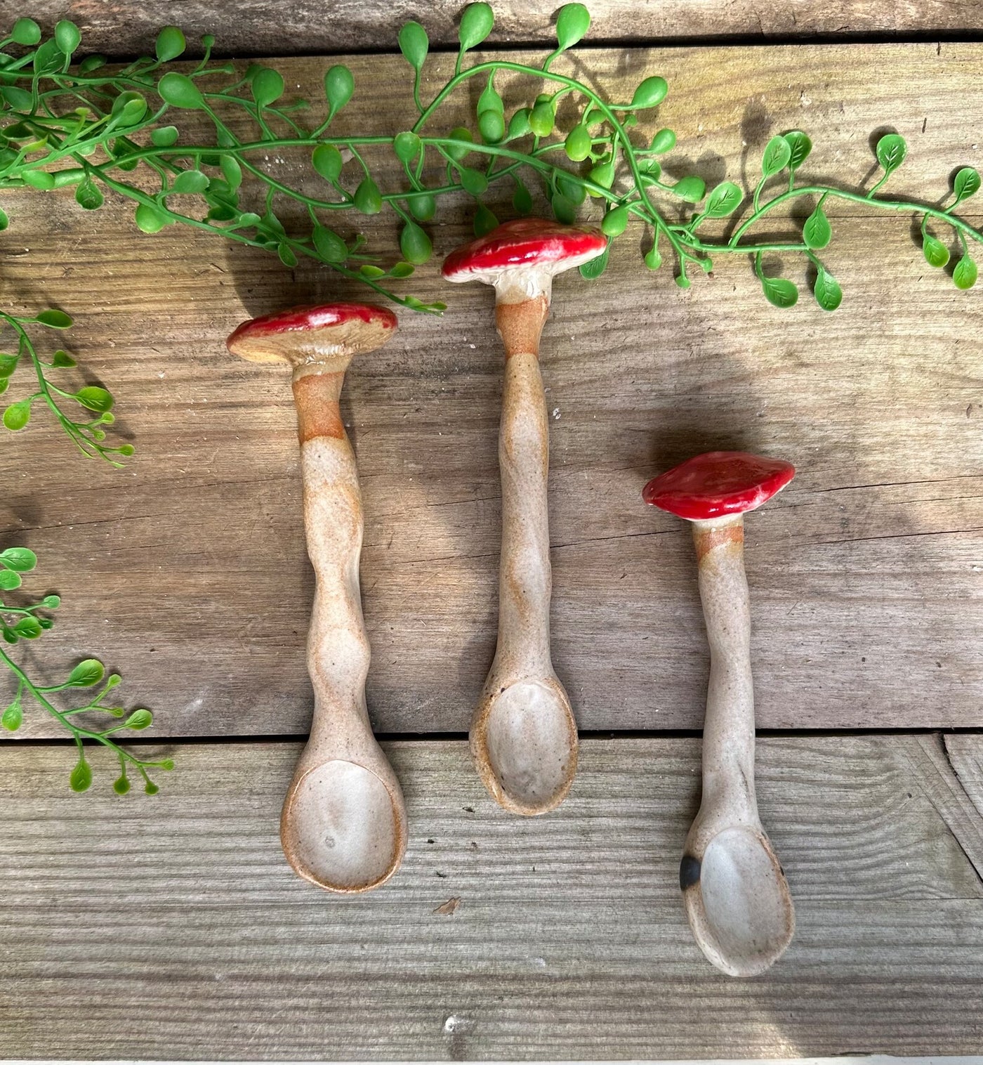 Three ceramic spoons shaped like mushrooms on a wooden surface with green leaves.