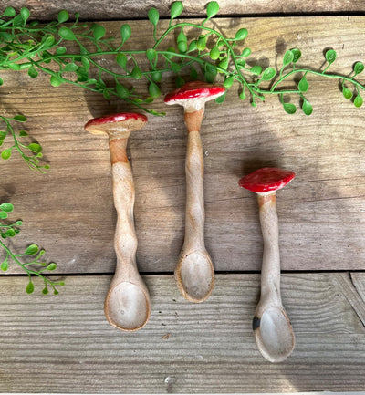 Three ceramic spoons shaped like mushrooms on a wooden surface with green leaves.