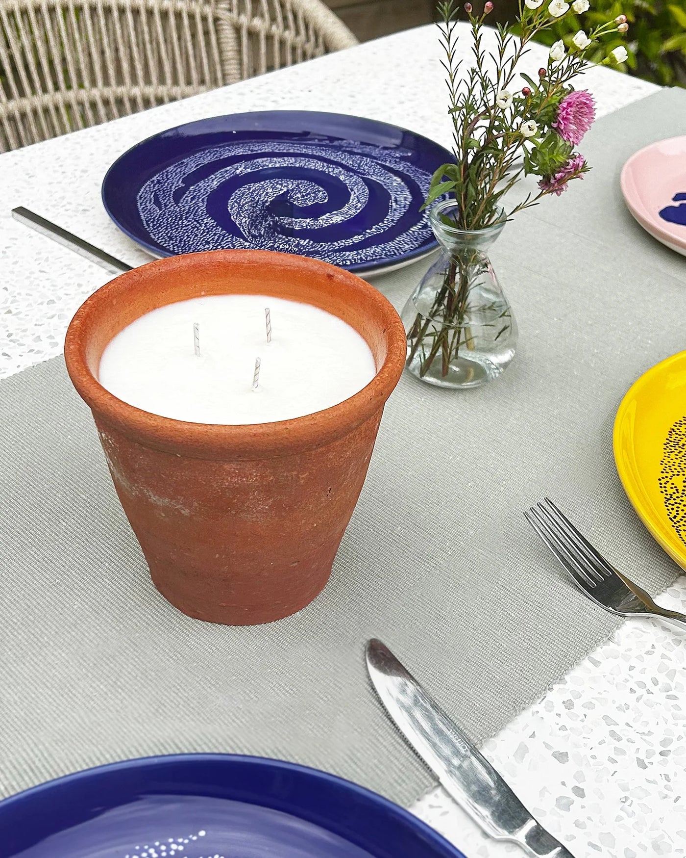 Candle in a terracotta pot on a table with plates and cutlery