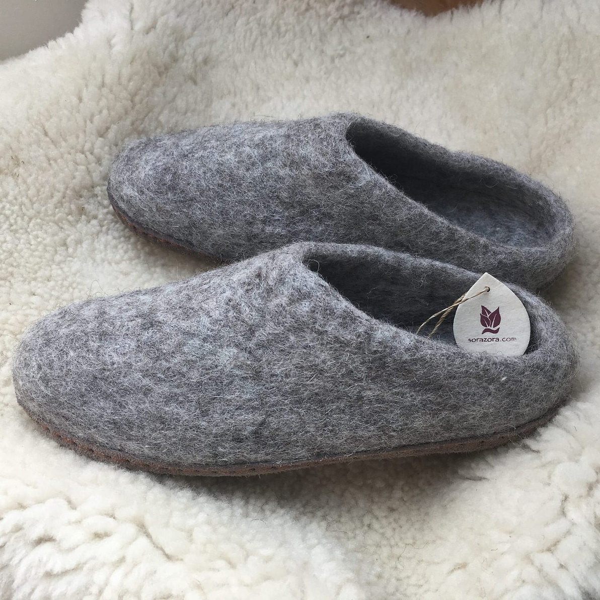 Pair of gray slippers with a tag on a soft white surface