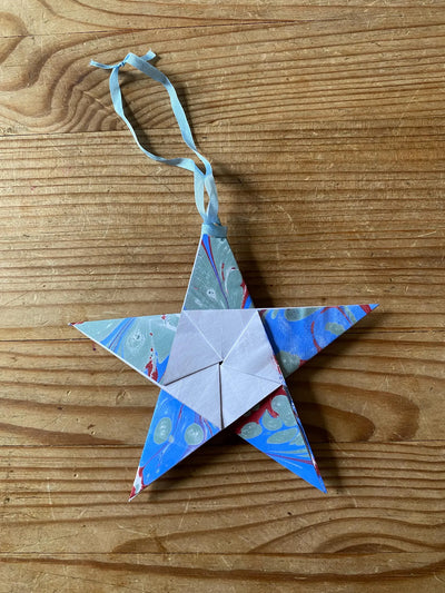 Origami star ornament with a ribbon on a wooden surface