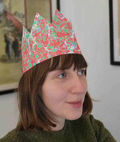 Person wearing a colorful paper crown indoors with a neutral background