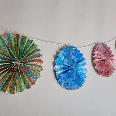 Colorful paper fan decorations hanging on a string against a plain background