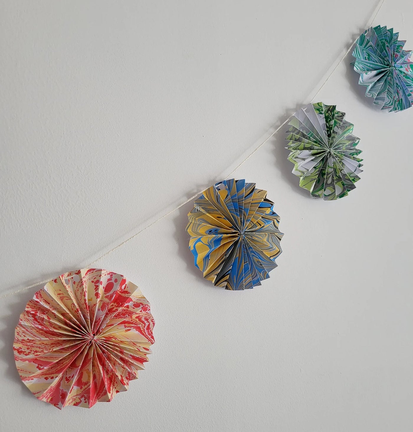 Decorative paper fans hanging on a string against a plain wall.