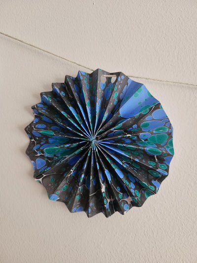Decorative paper fan with blue and black patterns on a plain background
