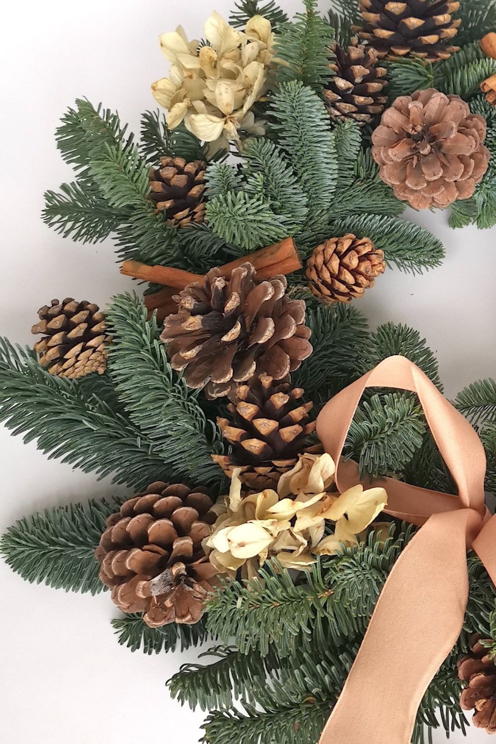 Decorative wreath with pine cones, gold balls, and a ribbon on a white background