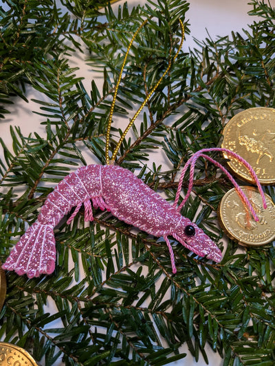 Pink glittery shrimp ornament on a Christmas tree with gold coins.