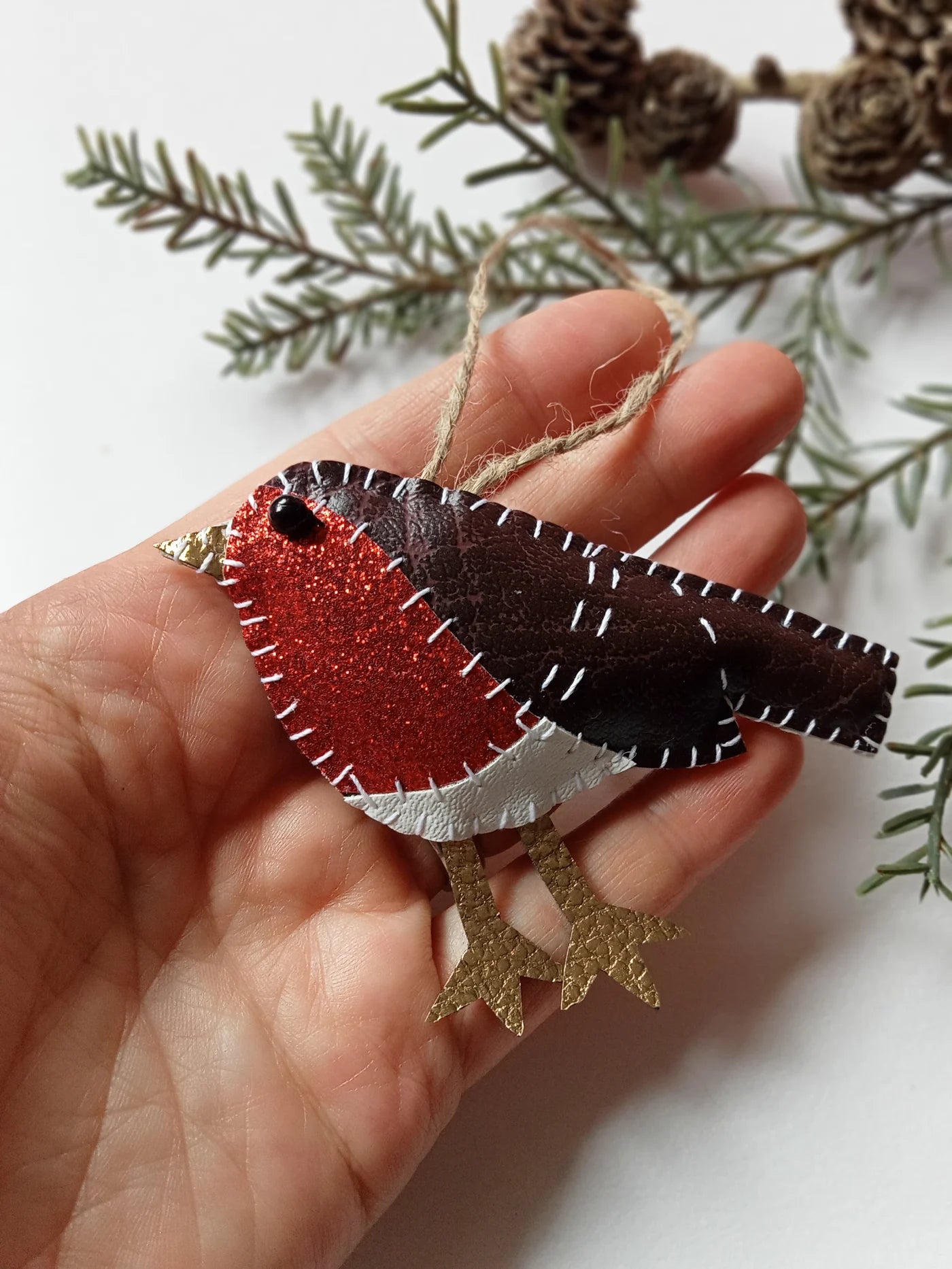 Hand holding a felt robin ornament with greenery in the background