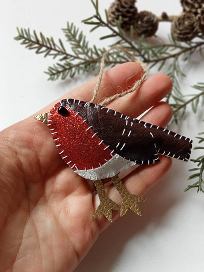 Hand holding a felt robin ornament with greenery in the background