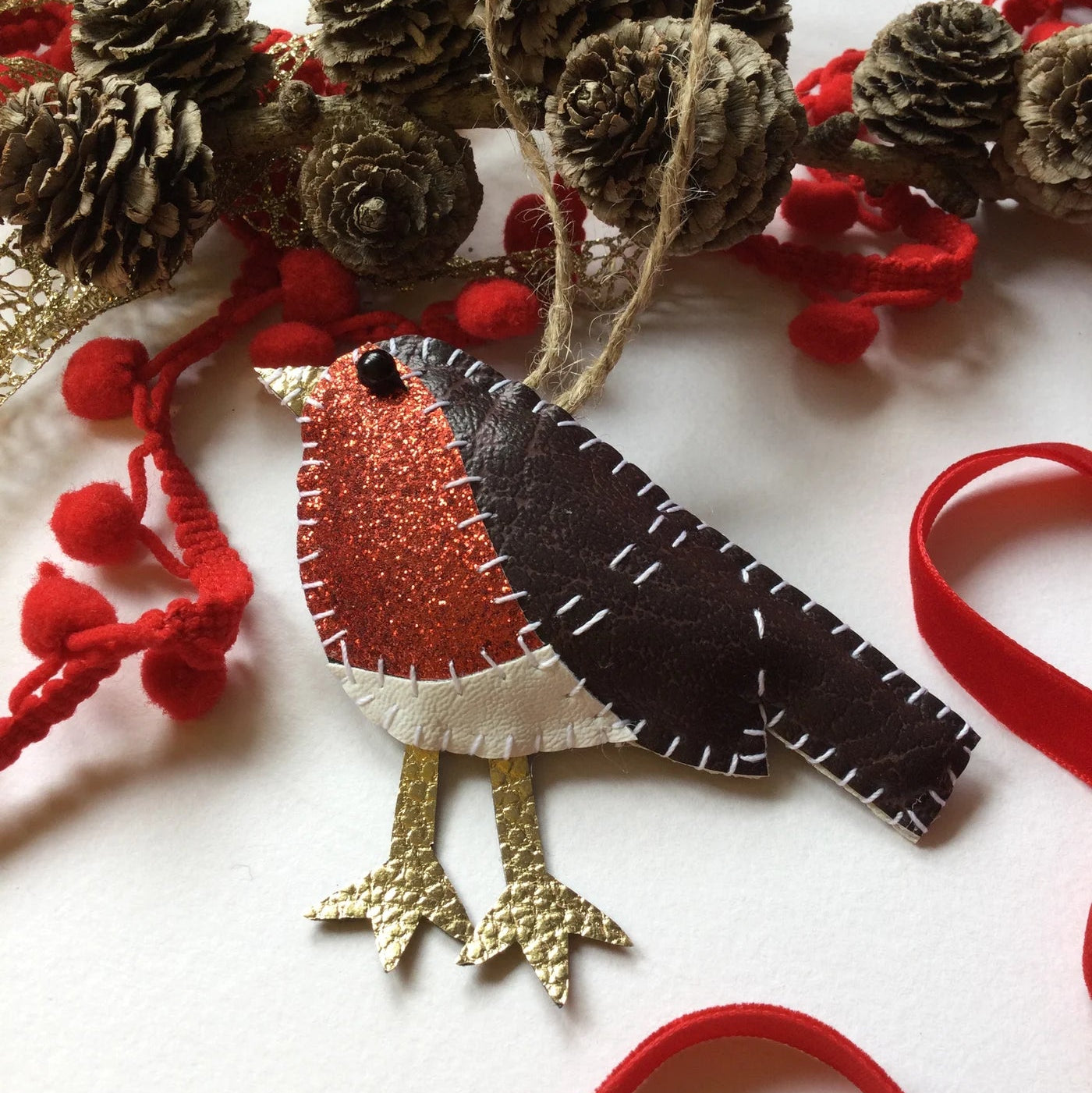 Felt robin decoration with pine cones and red berries on a white background