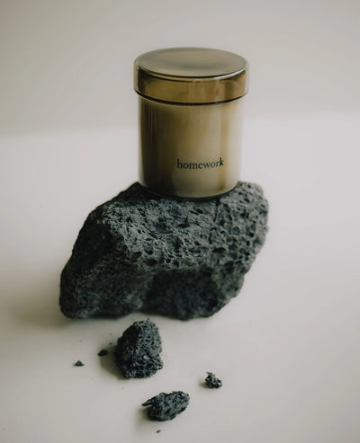 Metal canister labeled 'homework' on a rock with scattered rocks on a light background