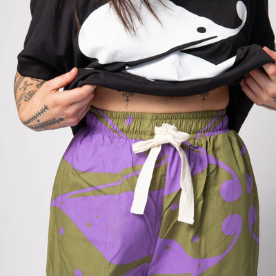 Person wearing a black crop top with a white whale design and green and purple pants with white drawstring.