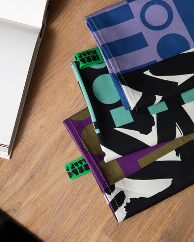 Three tea towels with colourful geometric patterns on a wooden surface