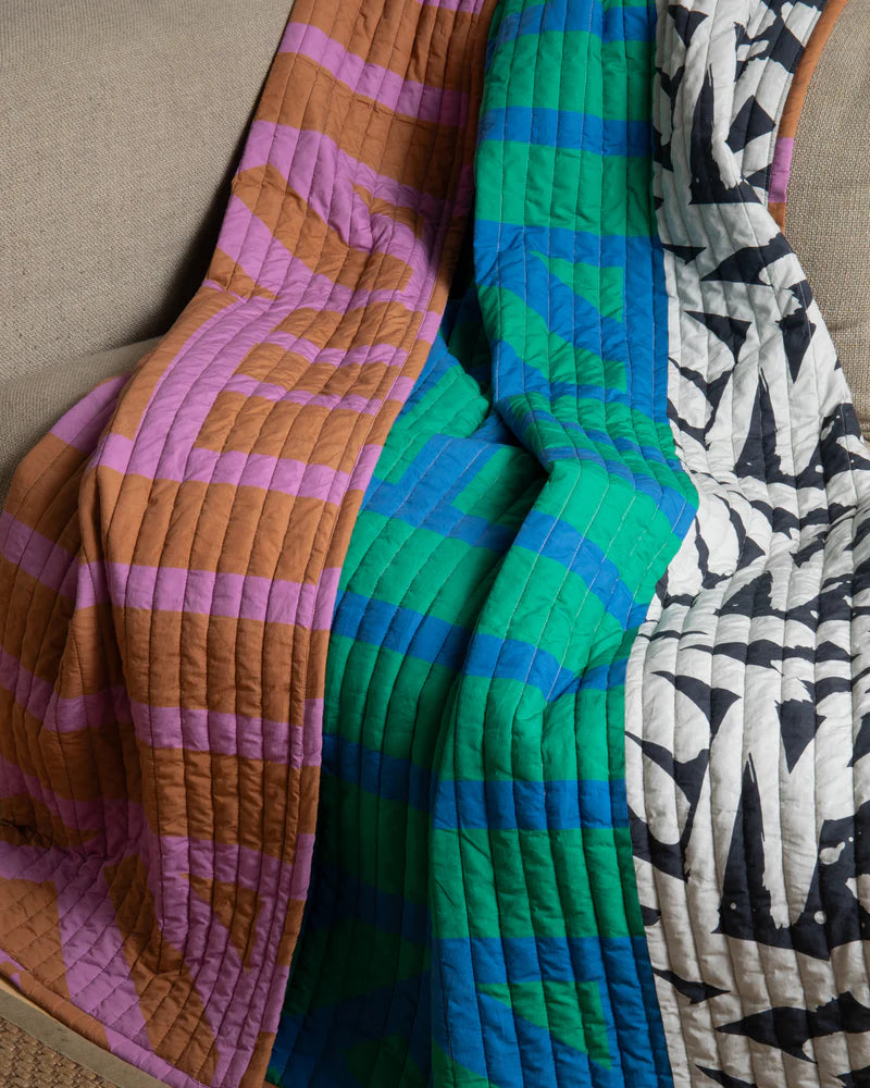 Three patterned quilts in different colors and designs draped over a surface.
