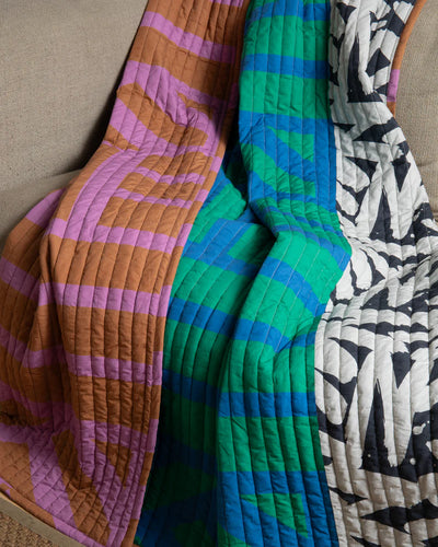 Three patterned quilts in different colors and designs draped over a surface.
