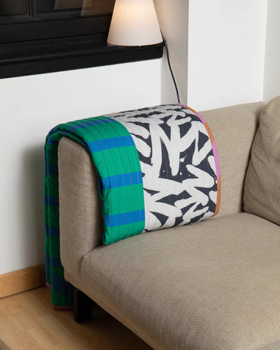 Colorful quilt draped over a beige sofa in a room with a lamp and white wall.