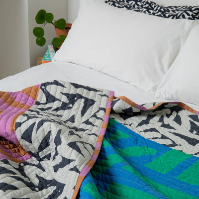 Colorful quilt with geometric pattern on a bed with white pillows.