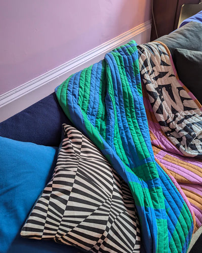 Colorful quilt draped over a couch with patterned cushions.