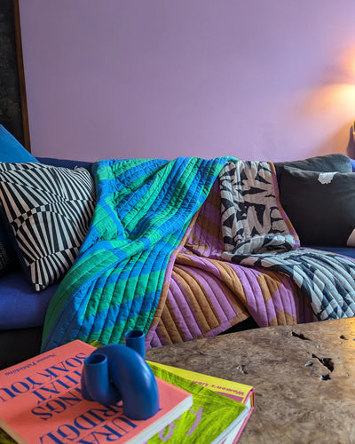 Colorful quilt draped over a sofa with books and a vase on a table in the foreground.