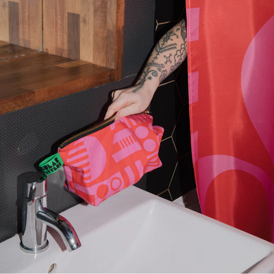 Person holding a pink patterned bag over a sink with a red curtain in the background